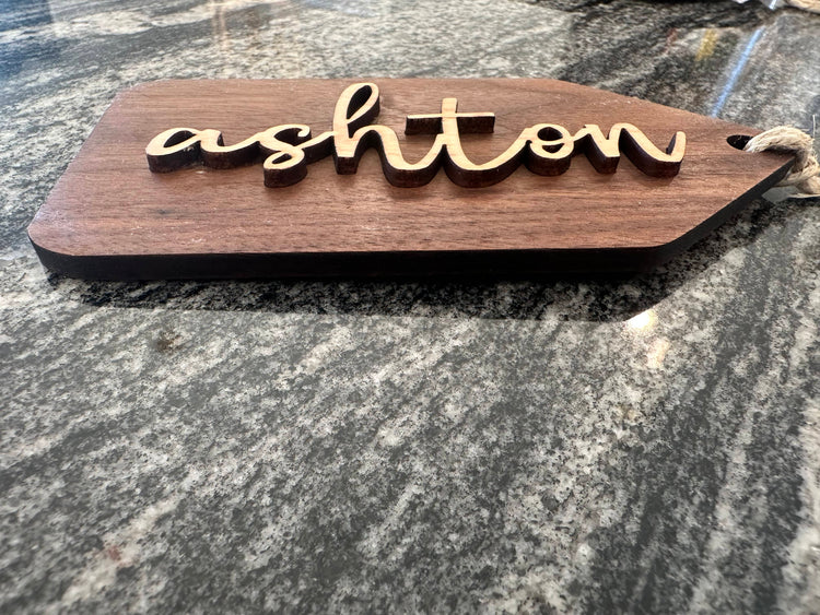 Wooden name tags/ stocking tags hanging on a Christmas tree with decorative lights.