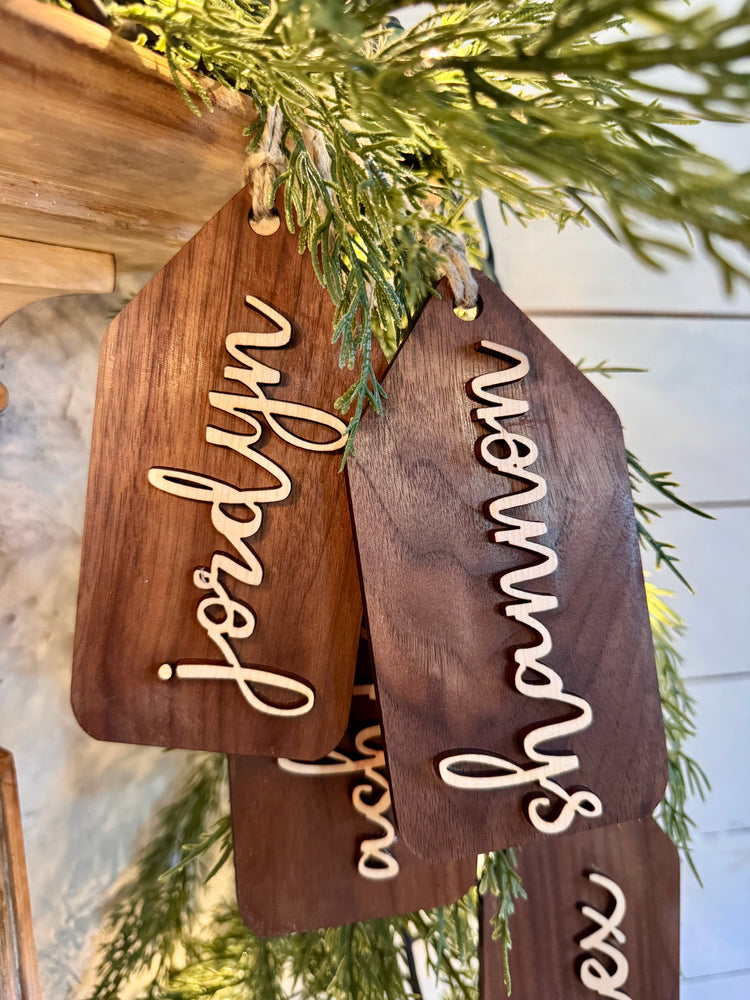 Wooden name tags/ stocking tags hanging on a Christmas tree with decorative lights.