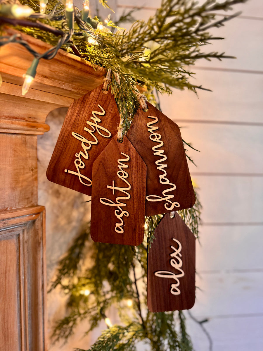 Wooden name tags/ stocking tags hanging on a Christmas tree with decorative lights.