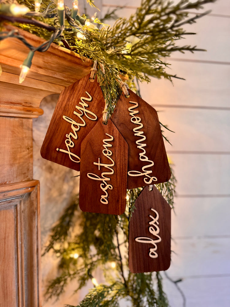 Wooden name tags/ stocking tags hanging on a Christmas tree with decorative lights.