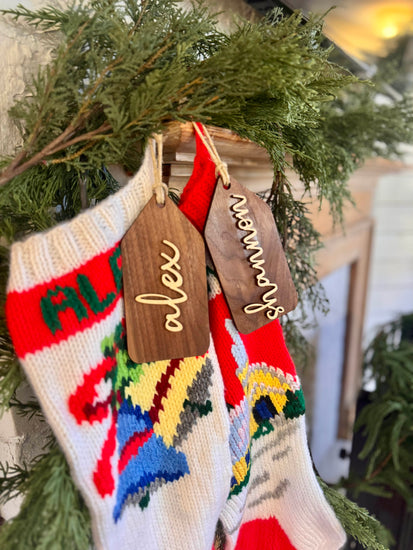 Wooden name tags/ stocking tags hanging on a Christmas tree with decorative lights.