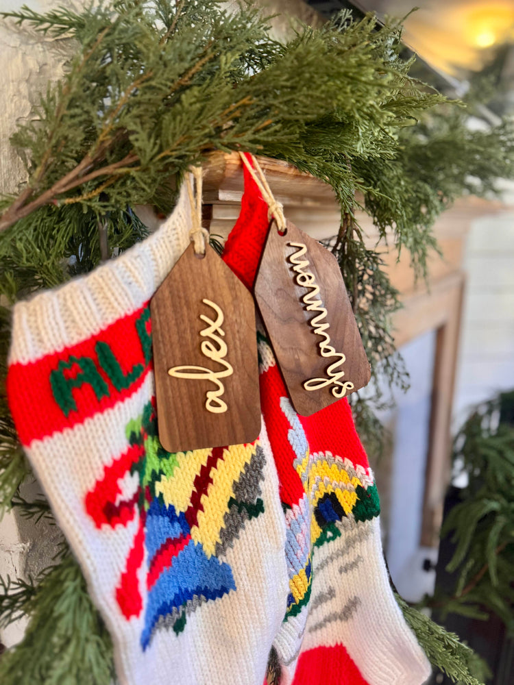 Wooden name tags/ stocking tags hanging on a Christmas tree with decorative lights.