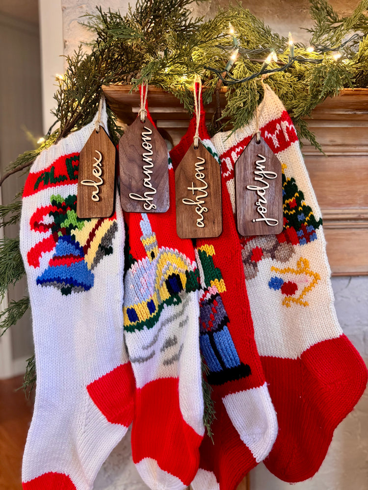 Wooden name tags/ stocking tags hanging on a Christmas tree with decorative lights.