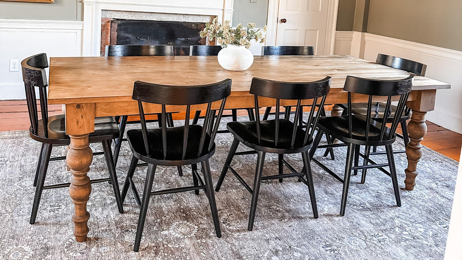 An eight-foot pine dining table surrounded by black chairs